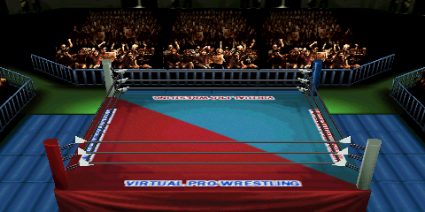 Screenshot of Nippon Budokan, focused on the
ring area. The upper middle portion contains cheering fans behind a row of guardrails.
Guardrails also appear on the left and right side, but disappear shortly due to the
perspective. A wrestling ring is the central focus, featuring a two-tone ring mat
design. The design is split on a diagonal, with the upper left portion being teal,
and the lower right portion being a dark red. 'VIRTUAL PRO-WRESTLING' text appears
on the four cardinal edges of the ring mat. The text has a white stroke, while the
fill color depends on the text location (blue fill for the red mat portion, red fill
for the cyan mat portion). Outside of the ring, blue padded mats appear to the left
and right. The outside corners are green and lack mats.